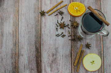 Hot mulled wine drink with lemon, apple, cinnamon, anise and other spices in a glass cup between fir tree branches on wooden cutting board
