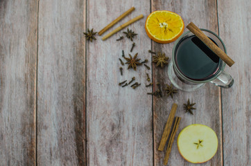 Hot mulled wine drink with lemon, apple, cinnamon, anise and other spices in a glass cup between fir tree branches on wooden cutting board