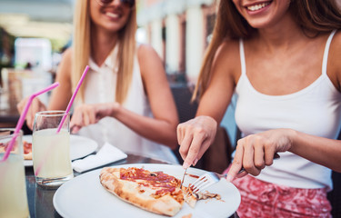 Pizza time. Young girls eating pizza in a cafe. Consumerism, lifestyle