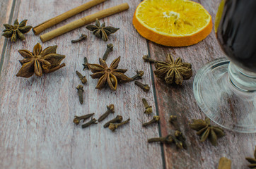 Hot mulled wine drink with lemon, apple, cinnamon, anise and other spices in a glass cup between fir tree branches on wooden cutting board
