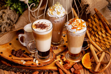Group of three hot layered coffee glasses decorated with whipped cream foam and nuts at xmas wooden table background.