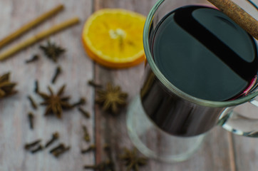 Hot mulled wine drink with lemon, apple, cinnamon, anise and other spices in a glass cup between fir tree branches on wooden cutting board