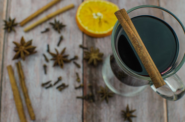 Hot mulled wine drink with lemon, apple, cinnamon, anise and other spices in a glass cup between fir tree branches on wooden cutting board