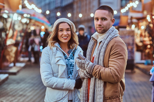 A young romantic couple walking on the street at Christmas time, standing near decorated shops in the evening, enjoying spending time together.