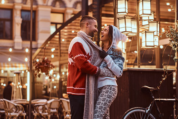 A young romantic couple wearing warm clothes hugging outdoor in evening street at Christmas time, enjoying spending time together.
