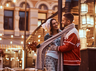 A young romantic couple wearing warm clothes hugging outdoor in evening street at Christmas time, enjoying spending time together.