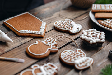 A lot of ginger biscuits in different form on brown wooden table. Decorated with white sweet glaze. Christmas mood, winter morning. Fir branches