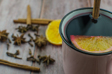 Hot mulled wine drink with lemon, apple, cinnamon, anise and other spices in a glass cup between fir tree branches on wooden cutting board