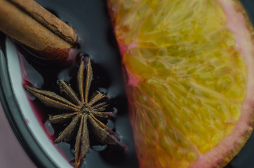 Hot mulled wine drink with lemon, apple, cinnamon, anise and other spices in a glass cup between...