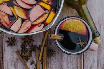 Hot mulled wine drink with lemon, apple, cinnamon, anise and other spices in a glass cup between fir tree branches on wooden cutting board