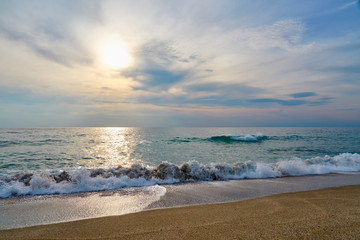 Sunset at the beach, waves with foam hitting sand.