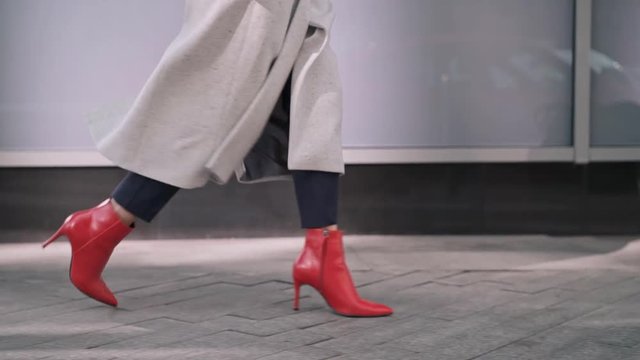 Legs of woman in red boots walking in autumn street
