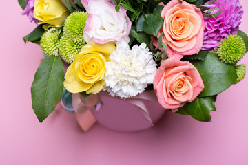 beautiful floral arrangement in the box, pink and yellow rose, pink eustoma, green and pink chrysanthemum, white carnation, pink dahlia on pink background with space for text.