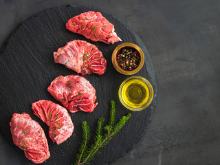 Raw pork cheeks meat on a dark gray background, top view with rosemary and spices. - obrazy, fototapety, plakaty
