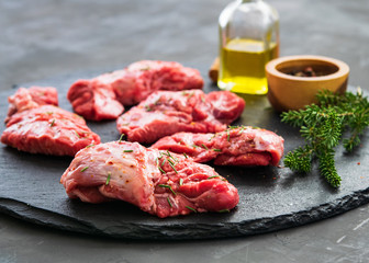 Raw pork cheeks meat on a dark background with rosemary and spices.