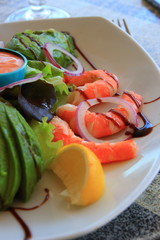 Plate of avocado, shrimps and raw vegetables with sauces on the table of a french restaurant