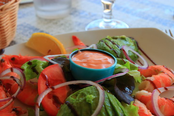 Plate of avocado, shrimps and raw vegetables with sauces on the table of a french restaurant