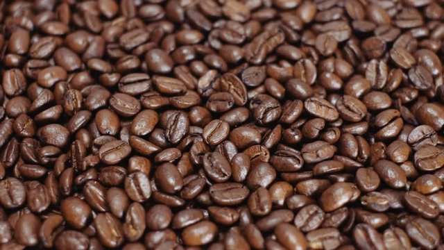 Whirling coffee grains loop background. Barista preparing fresh roasted coffee beans for making espresso. Morning black coffee texture. Close-up loop-able rotation of the heap of coffee beans.
