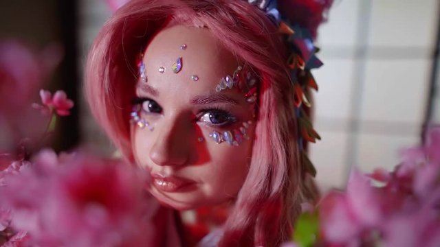 pretty model girl in creative image with pink hair, crystals on face, looking at camera through sakura