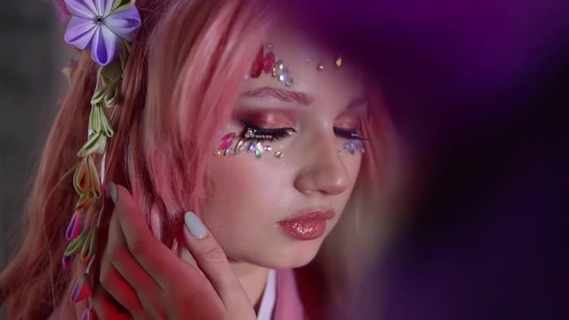 young pretty girl with pink hair and crystals on face is opening eyes and looking at camera