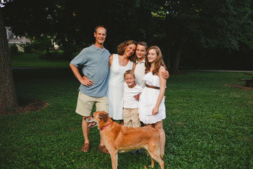 Portrait of smiling family with dog standing on grassy field in park