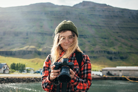 Young fashionable female tourist or photographer looks and inspects photos on digital dslr camera. Influencer or social media blogger creates content for blog on iceland roadtrip
