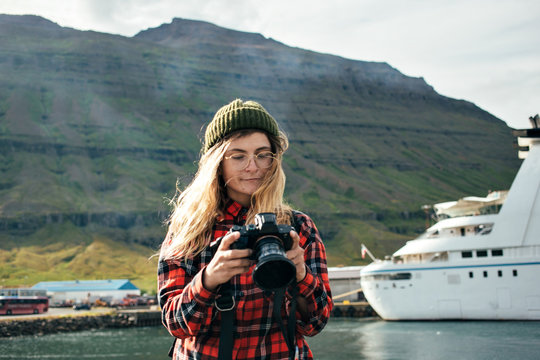 Young fashionable female tourist or photographer looks and inspects photos on digital dslr camera. Influencer or social media blogger creates content for blog on iceland roadtrip