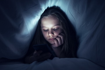 Young girl using a phone in bed