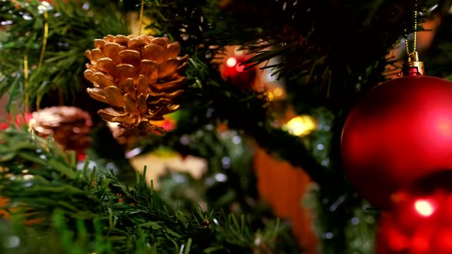 Decorated Christmas tree with red and gold balls and wooden Pinocchio toy. Dolly shot of Christmas holidays celebration. Blurred, sparkling and fairy background with green pine branches and cones.