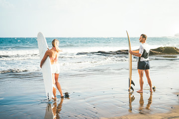 Young couple of surfers standing on the beach with surfboards preparing to surf on high waves -...