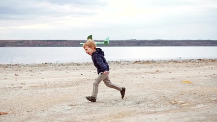 Happy child running with toy airplane and launching it in the sky. Kid boy playing with plane outdoors on nature. Little pilot dreaming of flight, having fun on vacation with family. Slow motion.