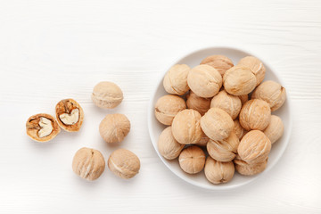Pile of walnuts on plate on white wooden background