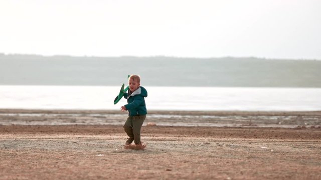 Funny kid boy epic fail of playing with plane outdoors. Happy child running with toy airplane and falls down to the ground. Little pilot dreaming of flight having fun on family vacation. Slow motion.