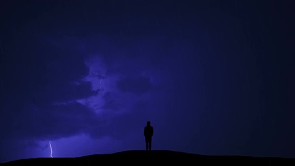 The man standing on the hill against the background of lightning
