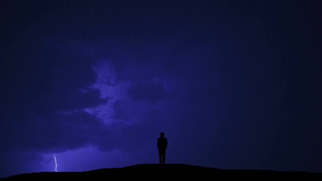The man standing on the hill against the background of lightning