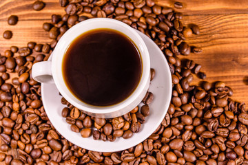 Cup of hot coffee and scattered coffee beans on wooden table. Top view