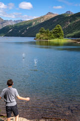 Boy skipping stones on lake in mountains