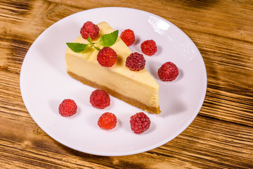White plate with cheesecake New York, leaf of mint and raspberries on wooden table
