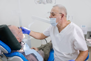 Adult dentist examines the oral cavity of his grandfather in a dental clinic