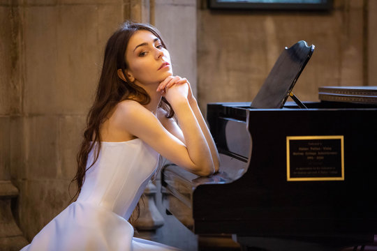 Beautiful Caucasian lady sitting at piano white dress