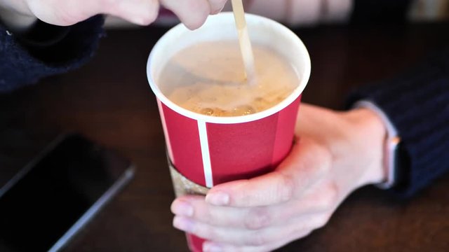Clip taken at coffee shop cafe of a caucasian women stirring a holiday coffee shop cup with hot coffee or tea in it. Shot in 4k 60fps and slowed down to 50% on a 30fps timeline.