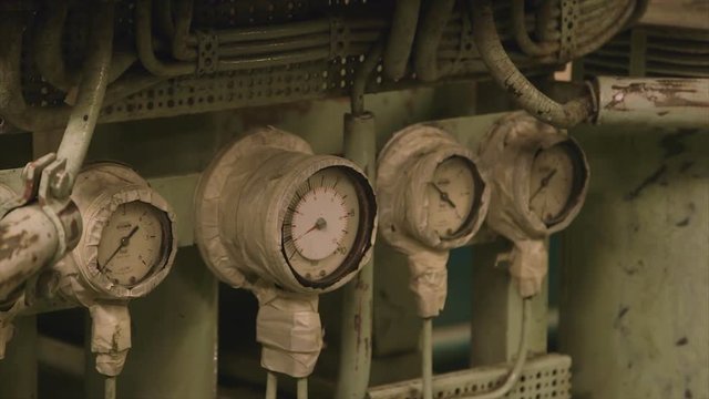 Close up steady shot, engine-room, four  engines pressure gauges, one bigger,  different readings, each covered by white masking tape except view glass window, multiple bending pipes, hoses,  pain