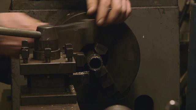 Extreme close up pan shot, old , rusty, grey painted lathe machine is switched on, machining, a shaft gear held in position by its chunk, stopped, technician, with unprotected hands, use vernier