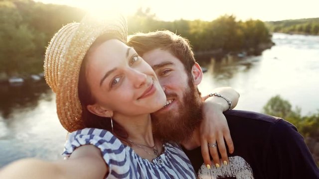 Happy couple travel, taking a self-portrait with smart phone camera on sunset. Loving man and woman making selfie for social media and nature landscape photo on romantic vacation outdoors.