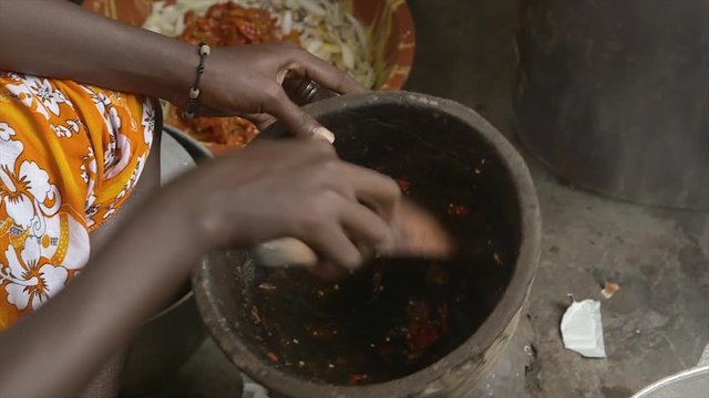 High angle pan, extremely close-up shot, young woman sitting, wear bracelet, white and orange coloured waist dress, collects paste of crushed spices from a wooden mortar for cooking, use a small flat