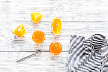 Fruit dessert. Orange jam in jar near slices of fresh oranges and spoon on white wooden background top view copy space