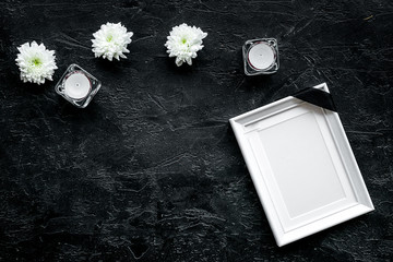 Death concept. Photo frame, mockup with black ribbon near flowers, candles on black background top view copy space