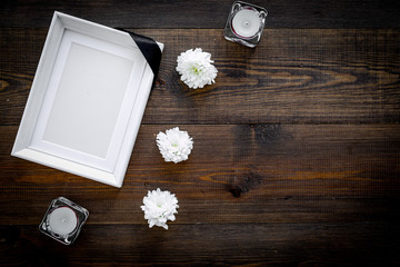 Death concept. Photo frame, mockup with black ribbon near flowers, candles on dark wooden...