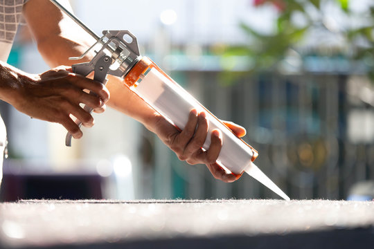 Men's hand uses silicone adhesive with a glue gun to repair worn windows.