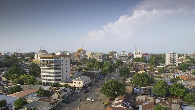 Wide still shot, aerial view of Conakry's main city road, highway, slummy rusty buildings, commercial, office flats scattered, tall green trees, calm, quiet street, parked vehicles, people walking